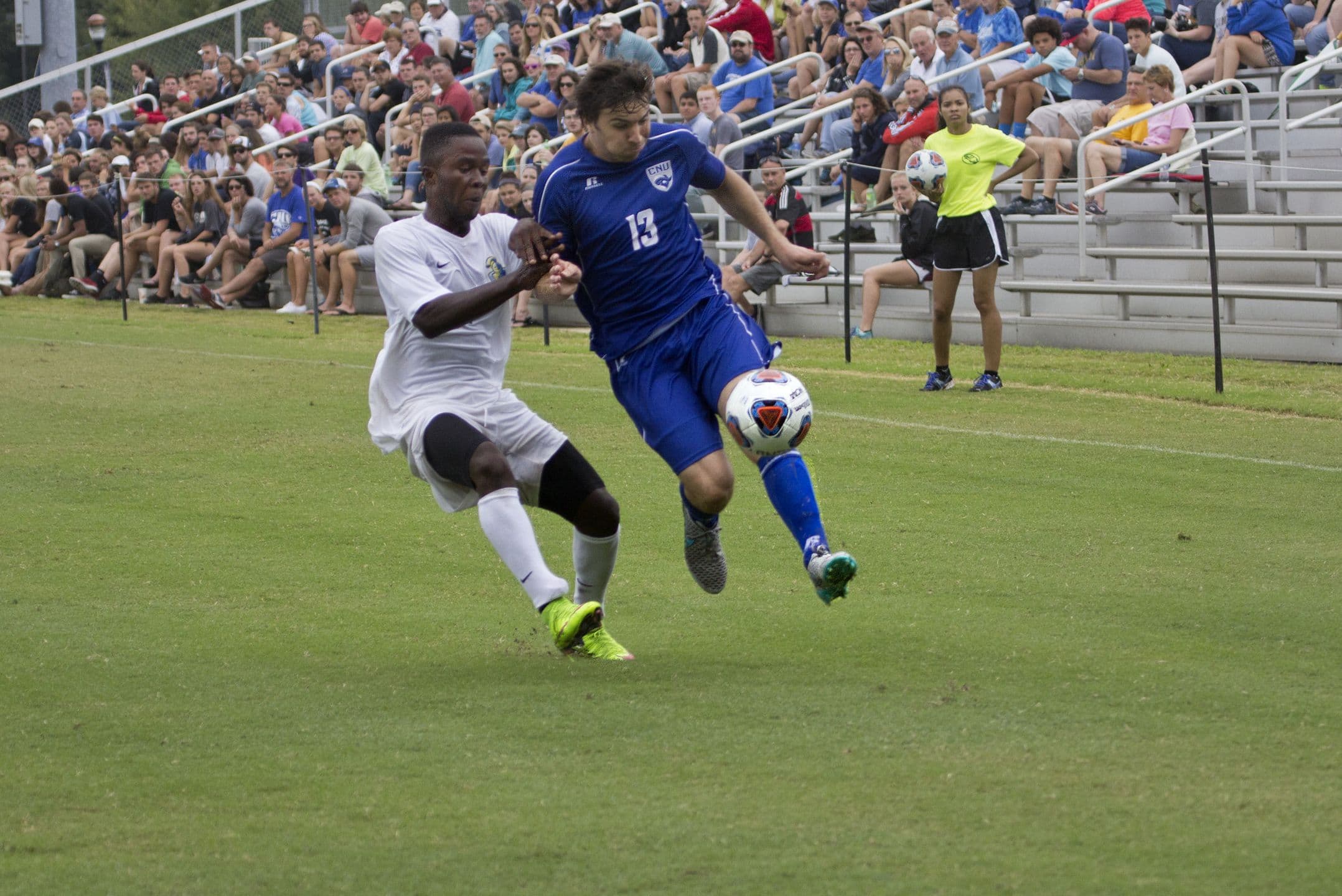 A Christopher Newport and a Neumann men's player racing for the ball in front of a home crowd