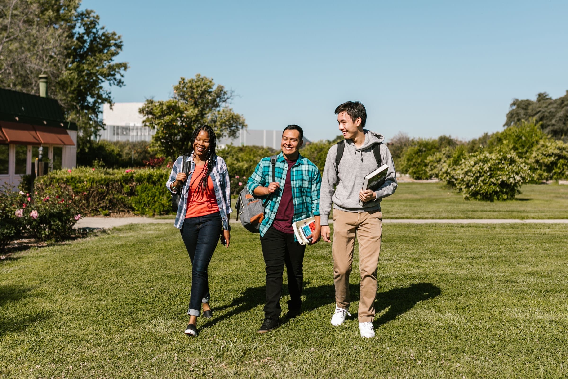 Three college students walking across a campus lawn
