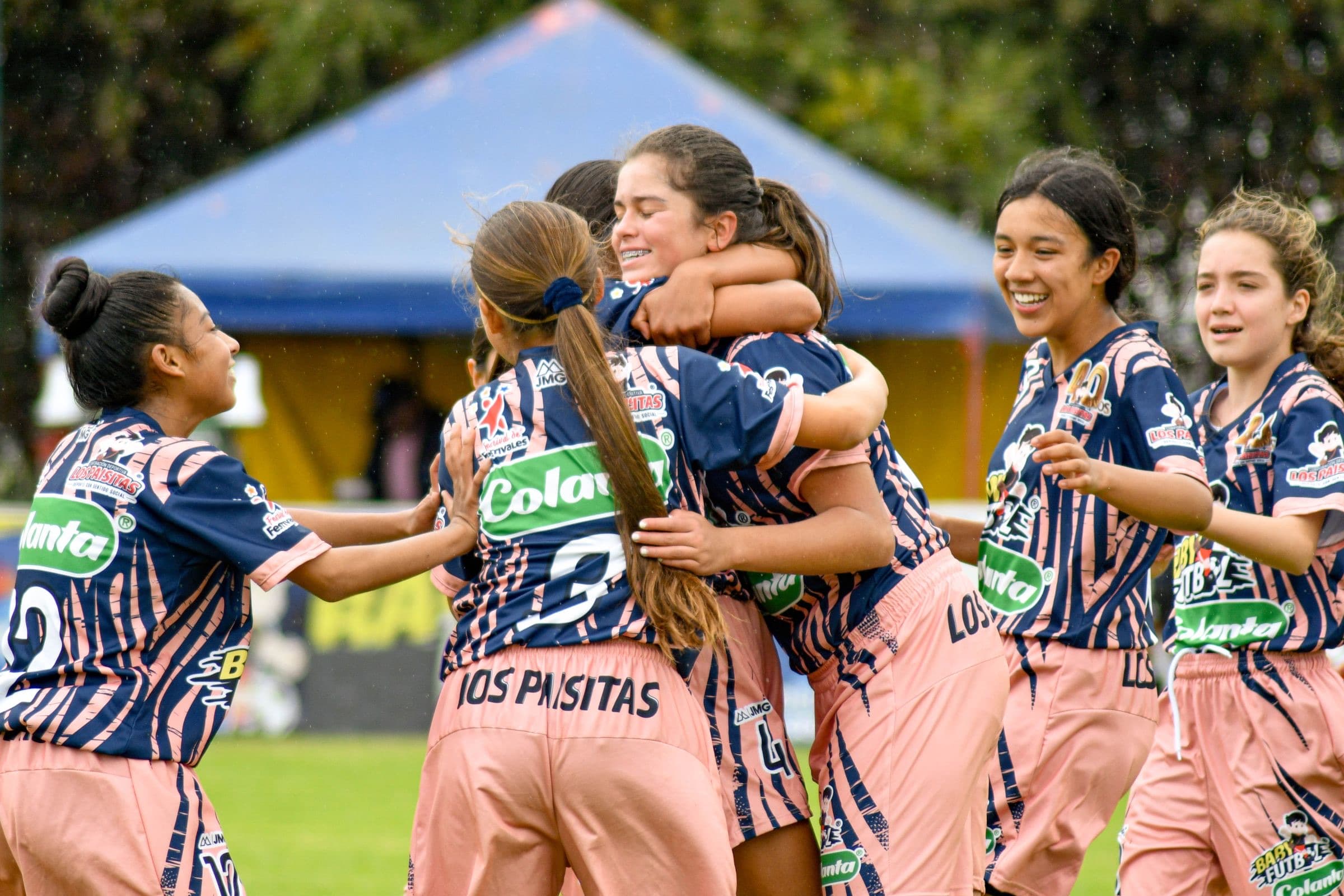 A girls' soccer team hugging and smiling on the field after a win